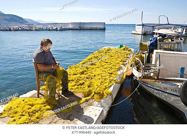 A fisherman mending nets on the quay side in the little harbour at Ayios Nikolaos, in The Outer Mani, Southern Peloponnese, Greece