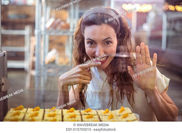 Pretty brunette looking at camera through the glass with finger in the mouth
