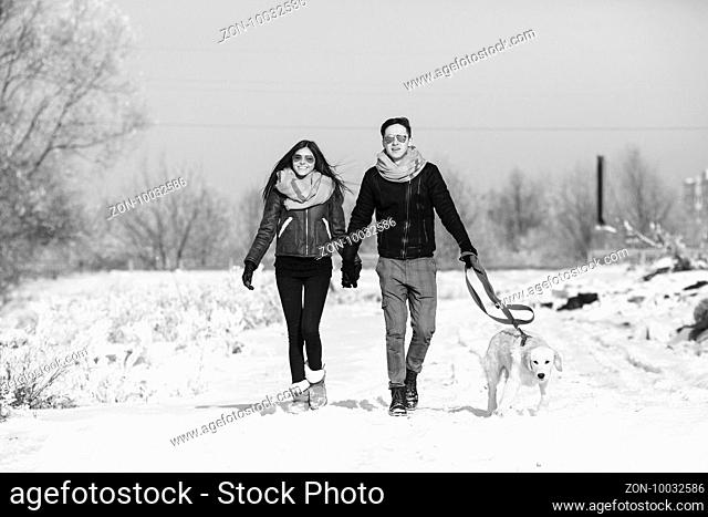 Young couple in love walking with dog outdoors in snowy winter