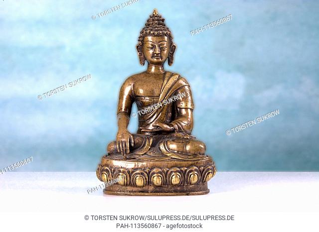 The bronze statue of a seated Buddha on a white background and against a mottled, neutral background. | usage worldwide. - /Deutschland