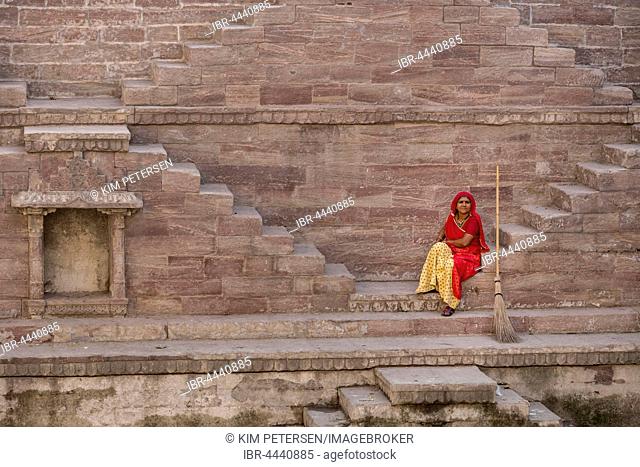 Woman in colorful sari resting on the steps at Toorji Ka Jhalara, The Step Well, Jodphur, Rajasthan, India