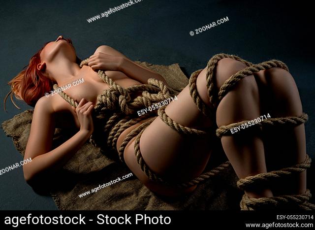 Girl tied up with a rope in shibari style lying on the floor in the dark room shot