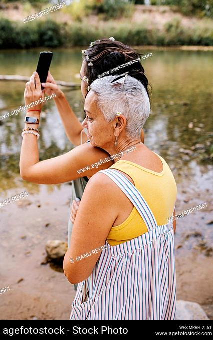 Women taking selfie through mobile at lakeshore