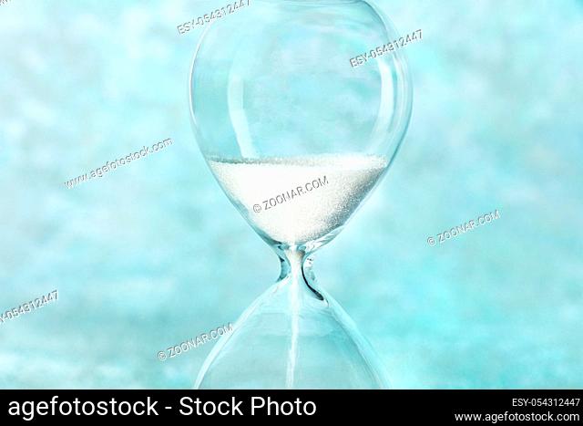 Time is running out concept. A close-up of an hourglass with sand falling through, on a teal blue background with a place for text