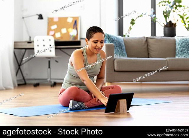 woman with tablet pc sits on exercise mat at home