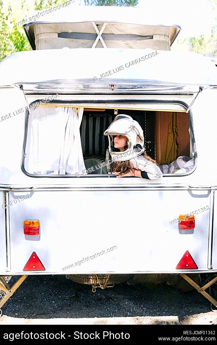 Girl wearing space suit looking through window while sitting in motor home