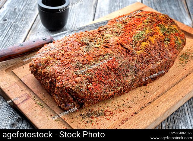 Traditional raw pulled pork piece of Bosten butt with spicy rub as closeup on a wooden cutting board