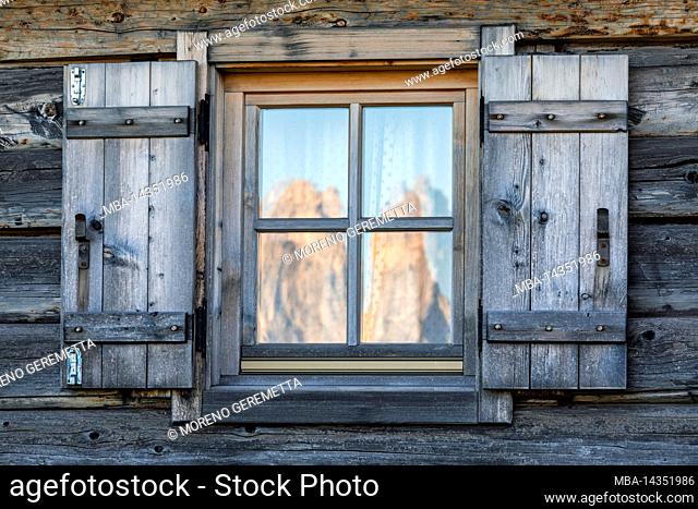 Italy, South Tyrol / Südtirol, Castelrotto / Kastelruth, Alpe di Siusi / Seiser alm - The window of a hut, on the glass the reflection of the Sciliar / Schlern...