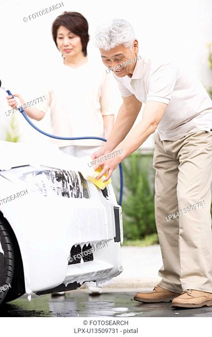 Senior couple washing car, using hose and sponge