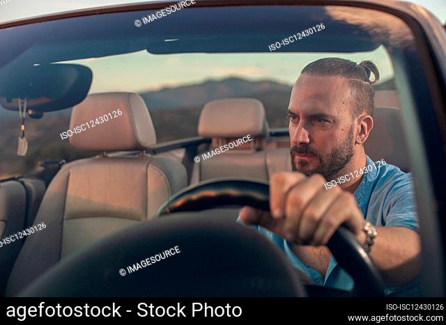 Man driving convertible car in landscape at sunset