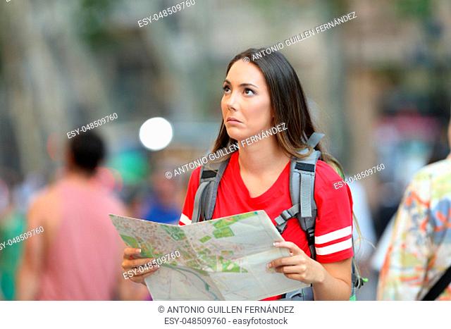 Confused teen tourist holding a paper guide looking above on the street
