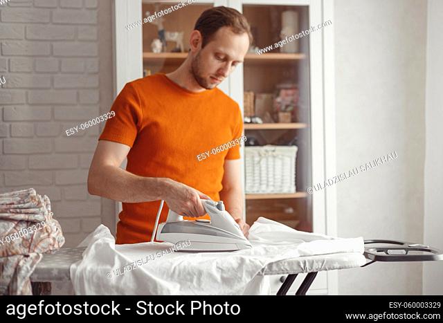 Young caucasian man ironing children's sheet on ironing board at home. Men doing home chores