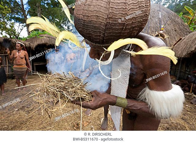 Dani man making fire in the traditional way under the eyes of the tribe during the rare pigs feast, the pinnacle of the social and religious life, Indonesia