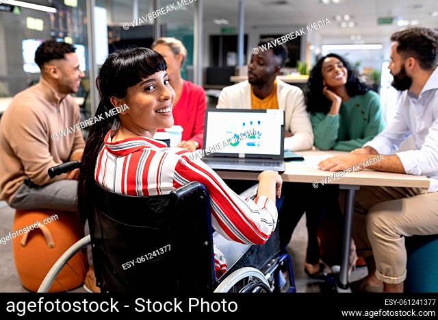 Smiling biracial disabled businesswoman looking over shoulder during meeting with colleagues