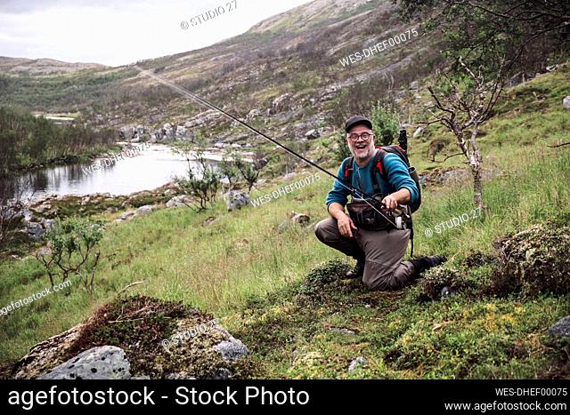 Laughing fly fisherman at river bank with mountains, Lakselv, Norway