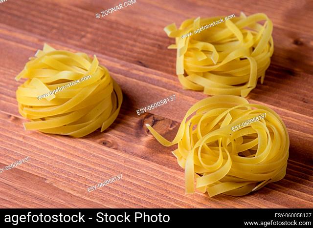 raw dry tagliatelle pasta on brown wooden table