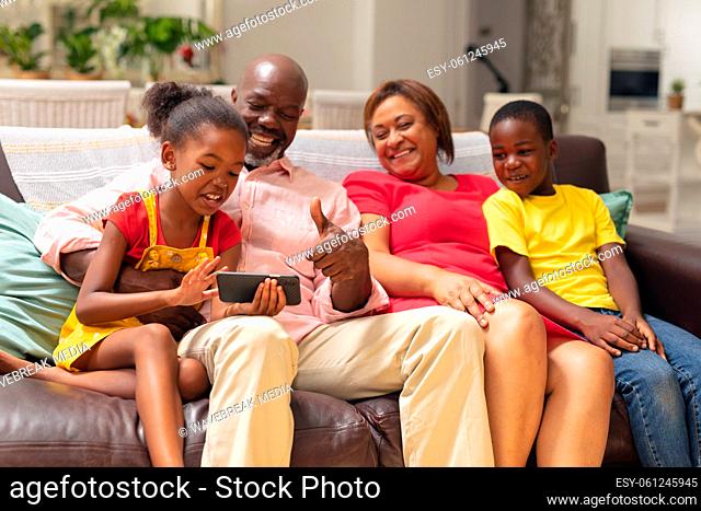 African american girl showing smart phone to brother and grandparents while sitting on sofa