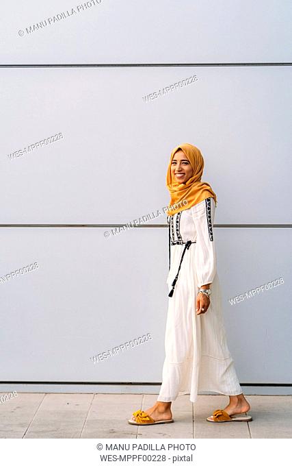 Young muslim woman wearing yellow hijab and walking in front of a white wall