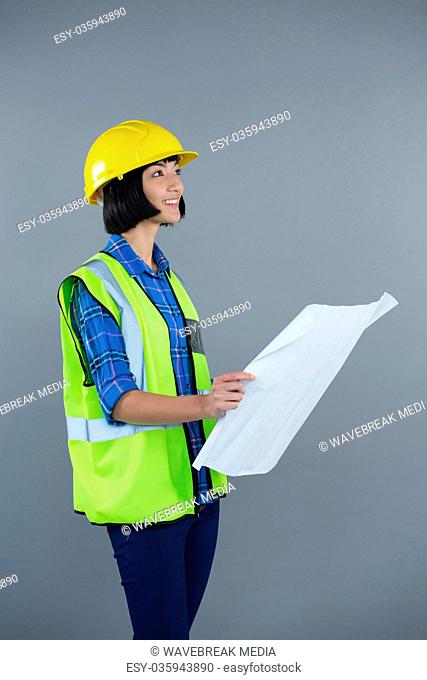 Female architect looking at blueprint against grey background