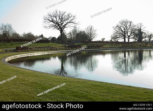 At dusk, Narcissus, copper beech hedges and Hellebores cluster along the bank and are reflected in the surface of the semi-circular lake beside the Glasshouse...