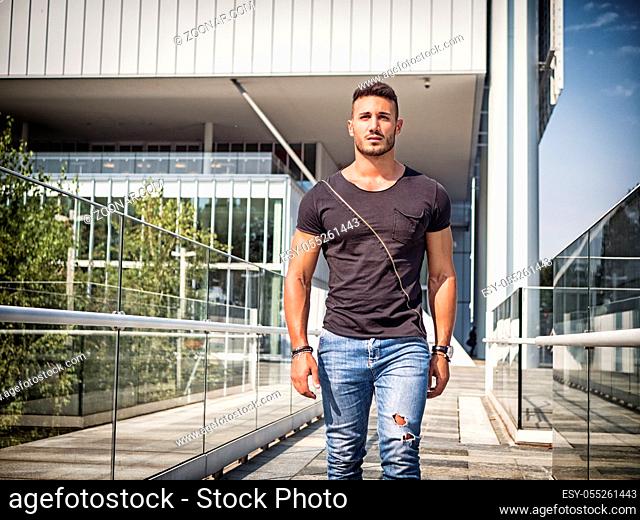 One handsome young man in urban setting in European city, wearing jeans and black t-shirt