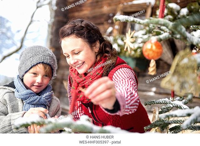 Austria, Altenmarkt-Zauchensee, woman and boy decorating Christmas tree in front of farmhouse