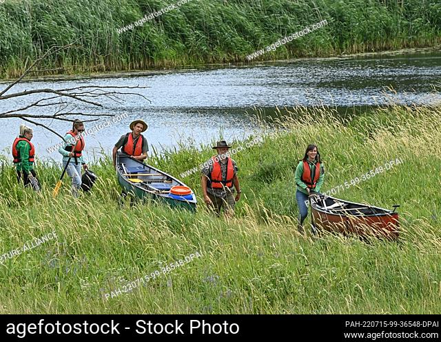 15 July 2022, Brandenburg, Schwedt/Oder: To start the 16th canoeing season in the Lower Oder Valley National Park, participants have to move their canoes from...