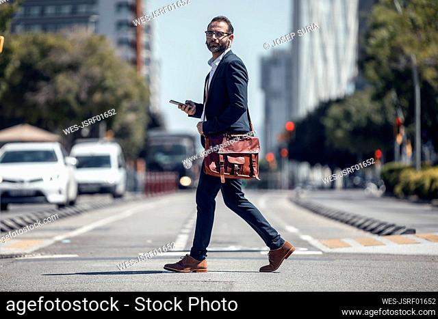 Male business professional with crossbody bag and mobile phone on street