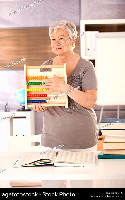 Senior teacher standing at desk, holding abacus, teaching math in elementary school