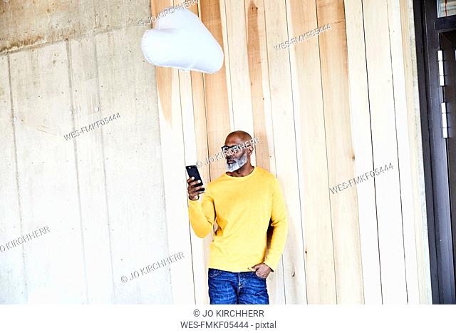 Mature businessman holding cell phone attached to cloud balloon