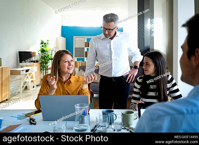 Businessman with hand on hip standing near colleagues discussing at office