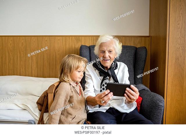 Portrait of aged woman watching together with her great-granddaughter photos on smartphone