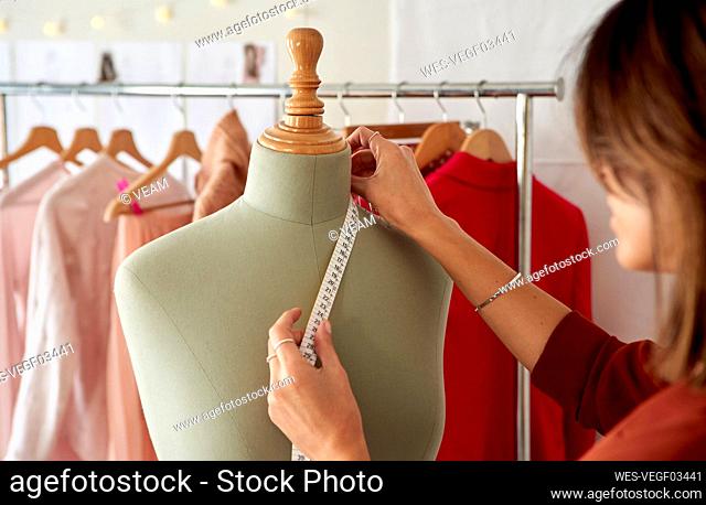 Fashion designer measuring dressmaker's model against clothes rack at design studio