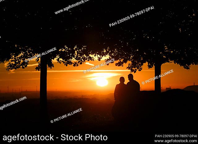 05 September 2023, Lower Saxony, Hanover: A couple sits on the Kronsberg at sunrise. Photo: Julian Stratenschulte/dpa. - Hanover/Lower Saxony/Germany