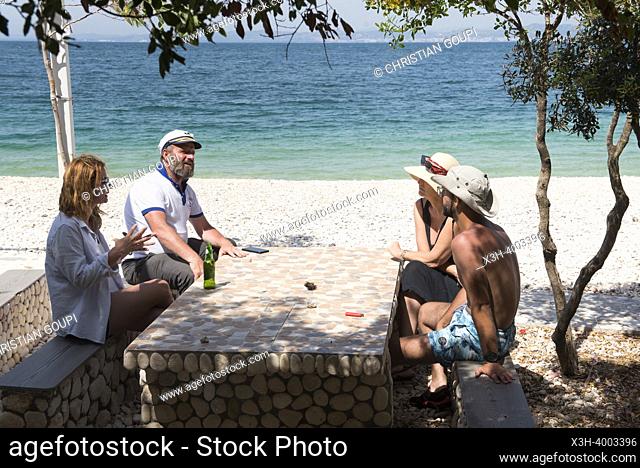 Four persons sitting at a table on the Beach in Zhanpovel Bay, Peninsula of Karaburun, within the Karaburun-Sazan Marine Parc, Vlore bay, Albania