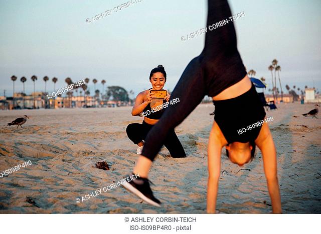 Friends photographing exercise on beach, Long Beach, California, US