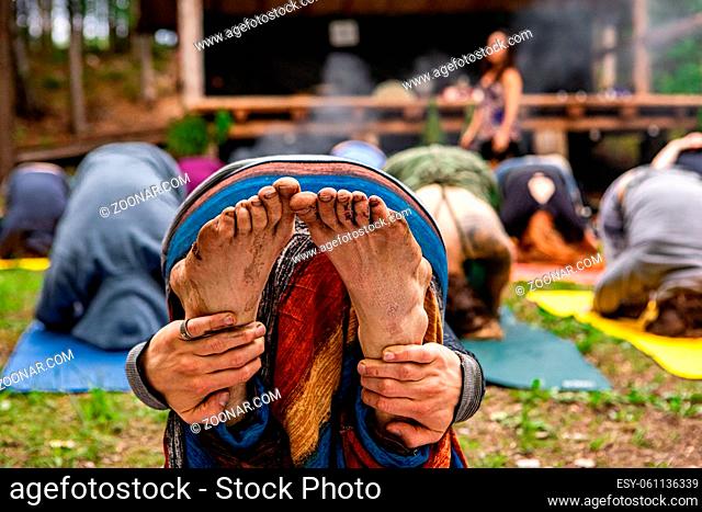 A closeup view on the dirty bare feet of a person meditating with a multiethnic group of people during a mindful woodland retreat