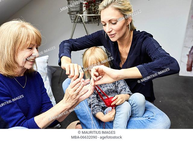 Grandmother, mother and little daughter at home, play with wool