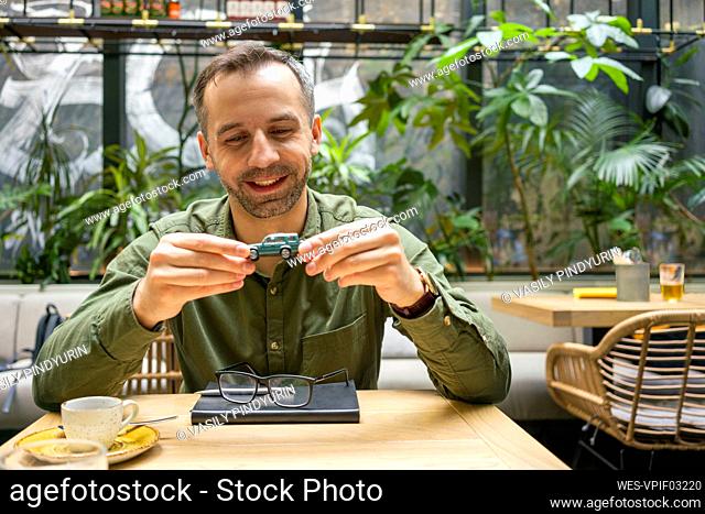 Smiling businessman holding toy car while sitting at cafe