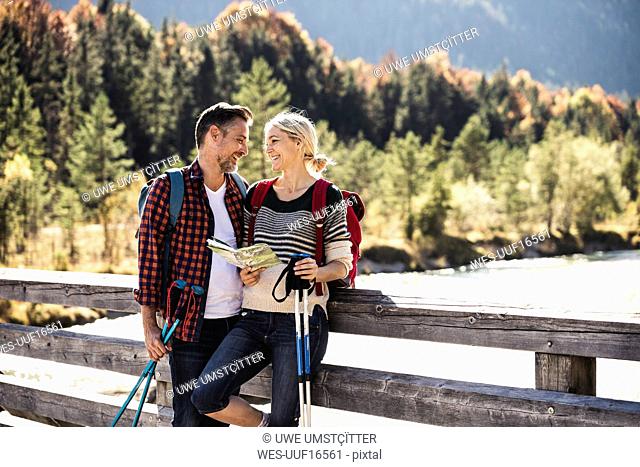 Austria, Alps, happy couple on a hiking trip with map on a bridge