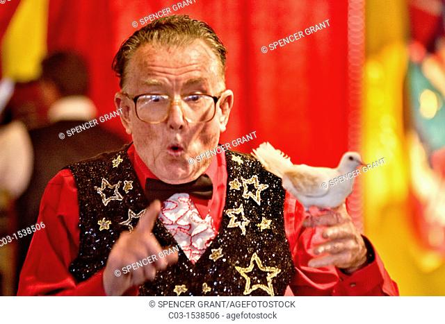 An elderly magician performs a 'disappearing dove' act in the amusement park the Orange County Fair in Costa Mesa, CA