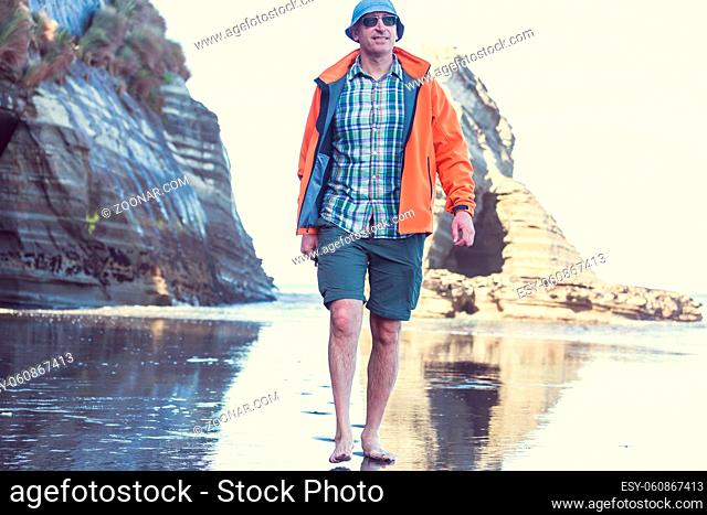 Tourist walking on the beach in the Three Sisters rock formation by New Plymouth coast, New Zealand