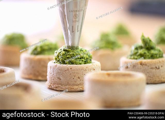 06 April 2023, Saxony, Dresden: A master baker fills round dough molds made from field bean flour with a pea and wild garlic paste at the ""Qioback"" bakery