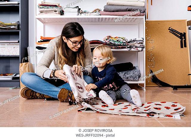 Mother and little daughter sitting on the floor at home checking fabrics