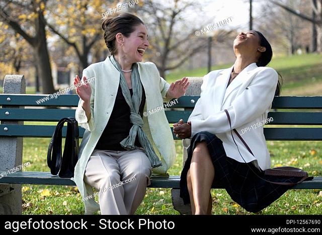 Two women sitting on a bench in the park and laughing