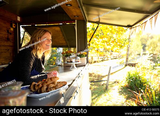 Happy female food cart owner in sunny autumn park