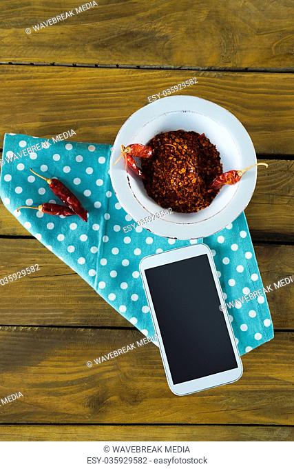 Hand holding mobilephone and chilli flakes in bowl