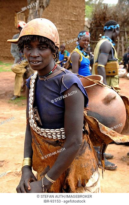 Woman wearing a chain of kauri mussels and a kalabasse on her head carries a big clay pot on her back on the market of Keyafer Ethiopia