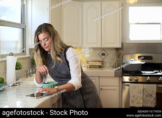 Young woman in her kitchen while eating breakfast getting on her iPad