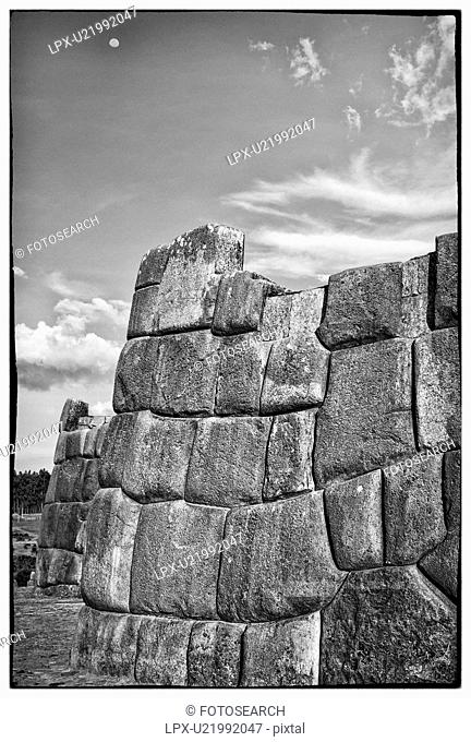 Sacsaywaman Inca ruins: monochrome close up view of the massive zig zag stone wall fortifications, with moon rising beyond, Sacred Valley, Cuzco, Peru